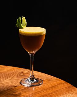 Cocktail with frothy top and lime garnish served on a wooden table at Toca Madera Scottsdale