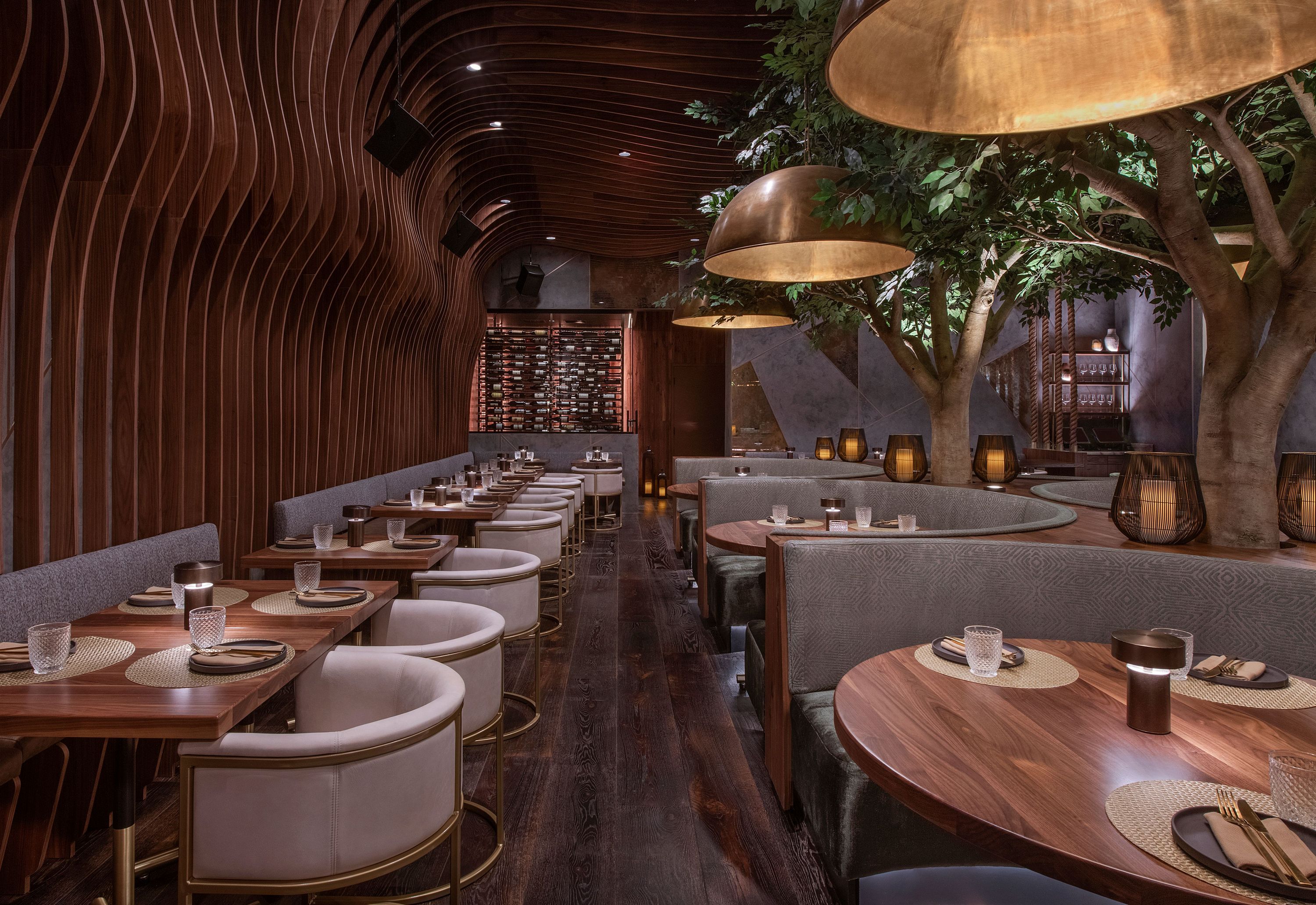 Dining area with curved wood walls, round wood tables, modern chairs, pendant lights, and built-in indoor trees