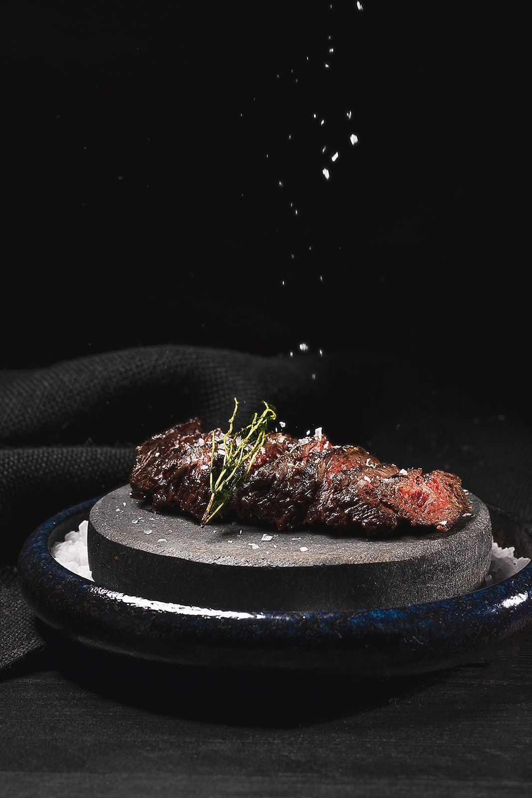 Grilled steak seasoned with salt and garnished with herbs, presented on a round black stone plate at Toca Madera Scottsdale.