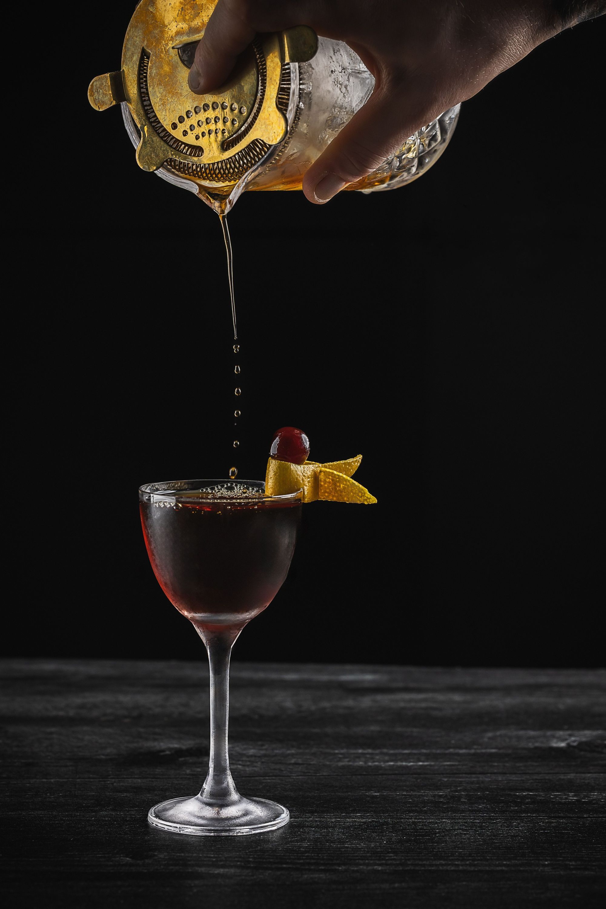 Cocktail being poured through a strainer into a glass with a cherry and citrus peel garnish at Toca Madera Scottsdale.