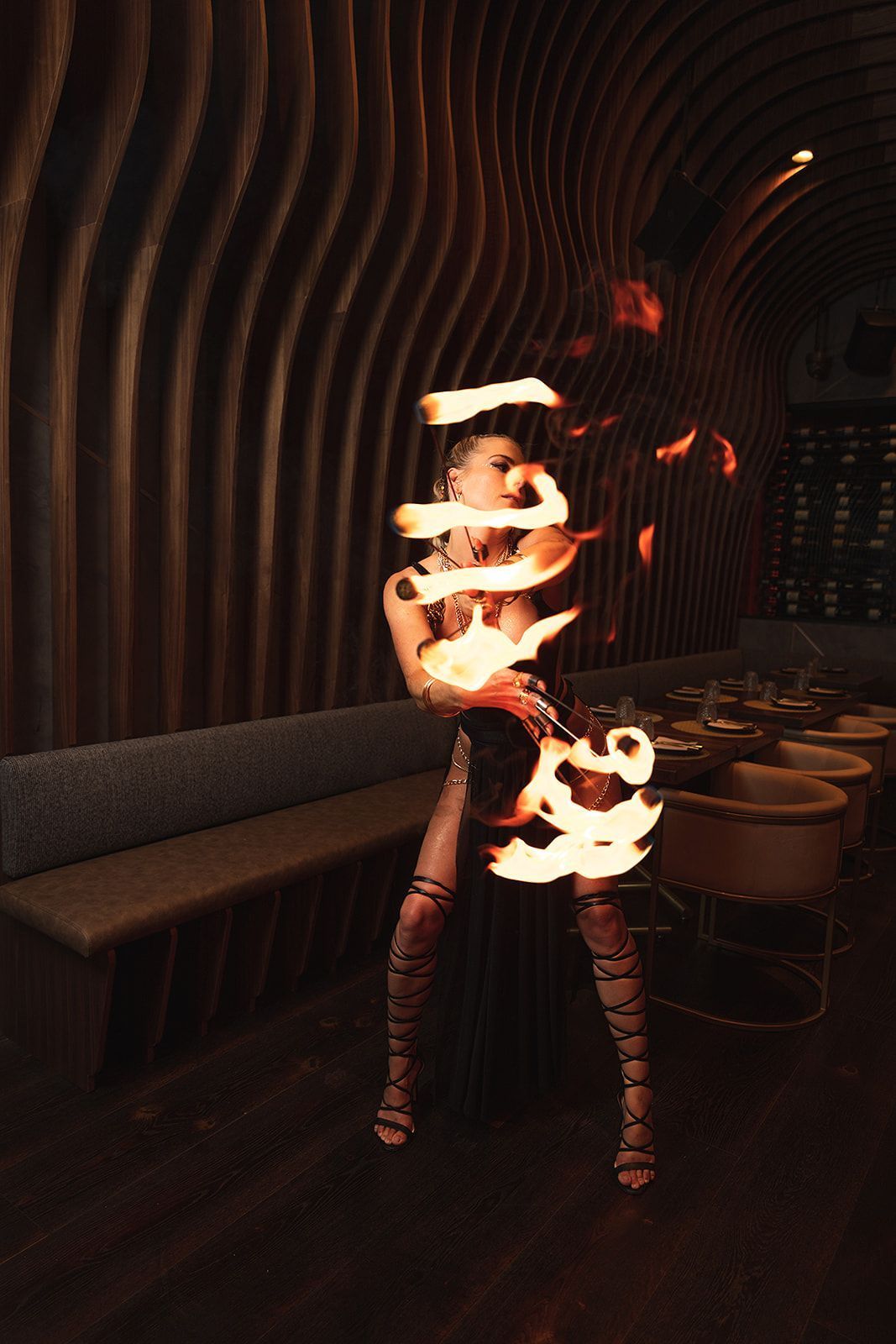 Person performing fire dancing inside Toca Madera Las Vegas with wavy wooden wall panels and modern dining seating.