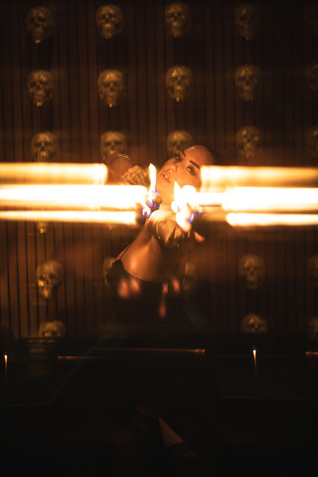 Dark interior with rows of skull decorations on the wall and a person performing with fire in the foreground.