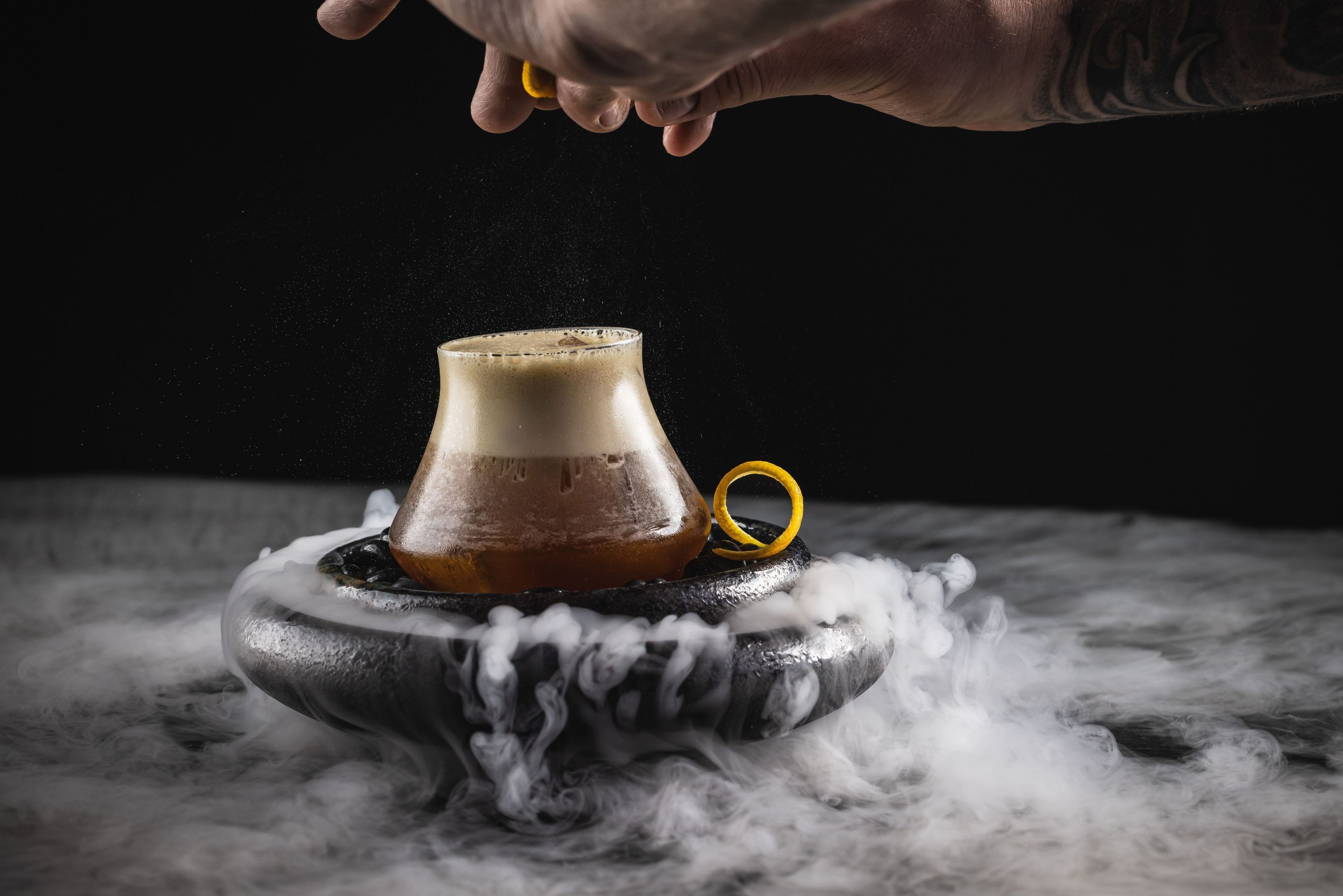 Mexican-inspired cocktail with foam and orange peel garnish served on a black smoky plate at Toca Madera Houston